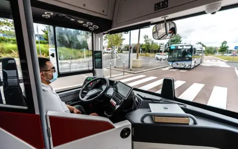 Vue de l'intérieur d'un bus RATP, le conducteur porte un masque. Un autre bus approche au loin.