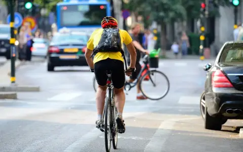 Un cycliste en tenue jaune et casque rouge profite de faire du vélo en ville, traversant une rue animée avec des voitures et un bus.