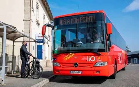 Un homme attend un bus LIO rouge à un arrêt, prêt à monter avec son vélo. Ce bus dessert les lignes comme Graulhet Gaillac.