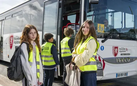 Trois jeunes, portant des gilets de sécurité fluo, attendent devant un bus scolaire de la Région Nouvelle-Aquitaine. La région vous transporte vers de nouvelles aventures.