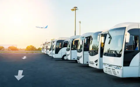 Une flotte de bus blancs alignés, prêts à transporter des passagers. L'avion au loin suggère la capacité d'un bus à relier les gens à leurs destinations.