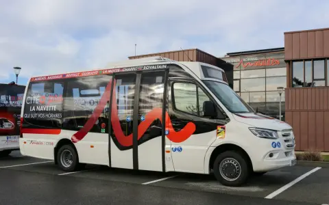 Un bus blanc avec des motifs rouges et noirs, portant l'inscription "Citéa La Navette" et des noms de localités, est garé devant un bâtiment "Valence Romans Mobilités".