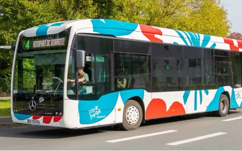Bus txiktxak Bayonne, ligne 4, direction Aéroport de Biarritz, avec un motif coloré bleu et rouge sur fond blanc.