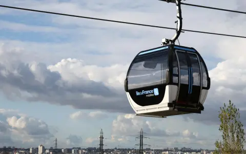 Cabine de téléphérique urbain en France, survolant un paysage urbain sous un ciel nuageux.