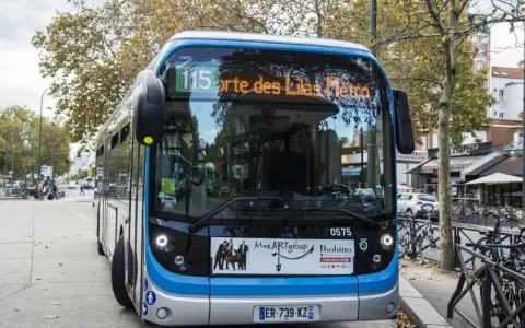 Bus Bolloré 115, direction Porte des Lilas Métro, stationné dans une rue bordée d'arbres et de commerces.