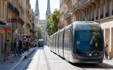 Un tramway moderne circule dans une rue pavée bordée de bâtiments anciens, témoignant du projet tramway urbain.