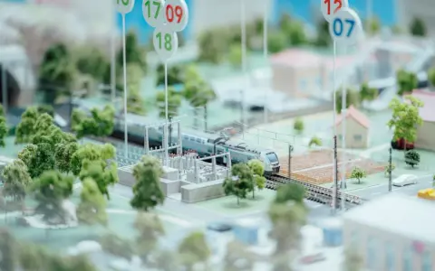 Maquette ferroviaire avec un train, des arbres et des maisons. Des panneaux indiquent des dates, peut-être pour un projet mobco 2026.