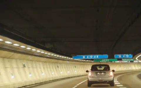 Voiture dans un tunnel éclairé, direction A10-A6 et A13. Un panneau indique Créteil et Versailles. Passage d'un duplex péage.
