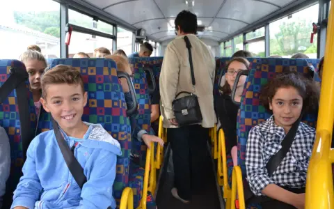 Des enfants souriants et une adulte voyagent dans un autobus scolaire aux sièges colorés.