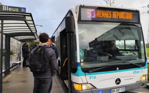 Un bus de transports urbains briochins s'arrête à un arrêt. Des passagers attendent, certains montent. Le panneau indique "53 Rennes République".