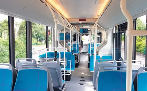 Intérieur d'un bus IDFM moderne avec des sièges bleus et gris, des barres de maintien et de grandes fenêtres donnant sur la verdure.