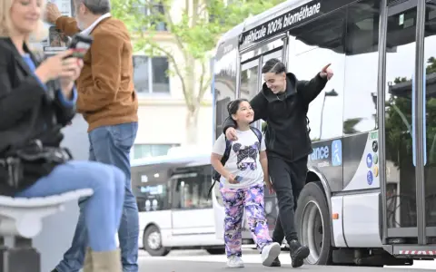 Un jeune homme et une fillette souriants marchent près d'un bus Transdev à Blois.