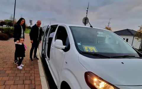 Famille attendant le transport scolaire communal. Le panneau jaune sur le pare-brise indique la présence d'enfants.