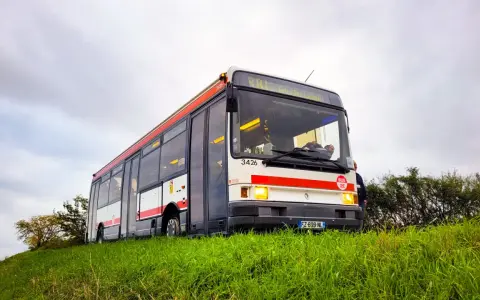 Un bus Renault R312 blanc et rouge, immatriculé FZ-609-NL, roule sur une colline herbeuse sous un ciel couvert.