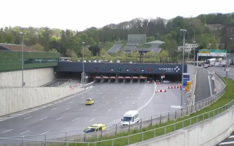 Entrée d'un **duplex autoroute** Vinci. Des voitures et des camions passent sous des portiques de péage.
