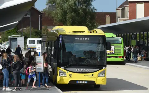 Des bus jaunes et verts attendent des passagers. Une affiche sur le bus vert mentionne "100% GRATUIT", illustrant la gratuité des transports en commun.