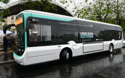 Un bus RATP bleu et blanc, "LIGNE 100% ÉLECTRIQUE", roule sur une chaussée mouillée.