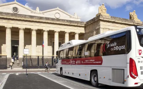Un bus blanc "car régionaux Gironde" roule devant un bâtiment imposant avec des colonnes. Le bus arbore le slogan "Je roule au bipgaz".