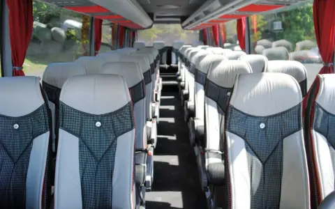 Intérieur d'un tour bus avec des sièges confortables et des rideaux rouges.