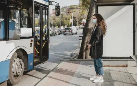 Une jeune femme avec un masque attend le bus, un moyen de déplacement pratique en ville.