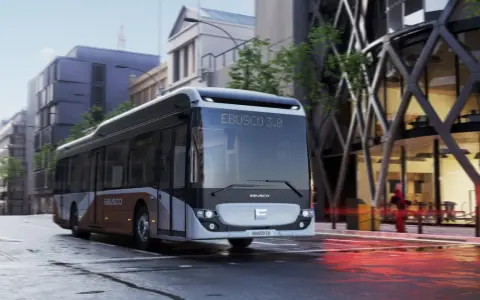 Un bus Ebusco 3.0 moderne circule dans une rue urbaine mouillée, reflétant les lumières de la ville.