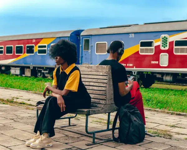 Deux personnes attendent sur un banc, un train coloré, un moyen de transport en Afrique, stationne derrière elles.