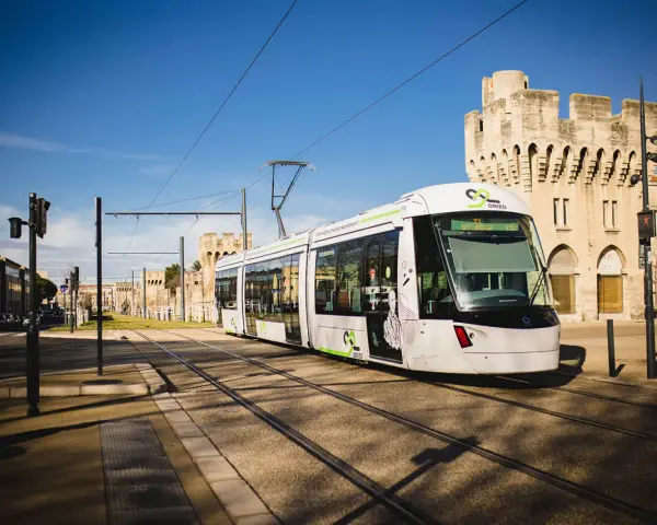 Le tramway moderne circule sur les rails à Avignon, passant devant des bâtiments historiques sous un ciel bleu éclatant.