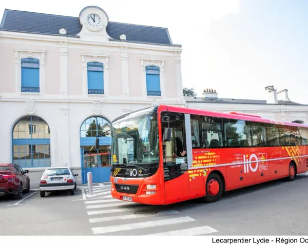 Un bus rouge Lio, service public Occitanie, s'arrête devant une gare.