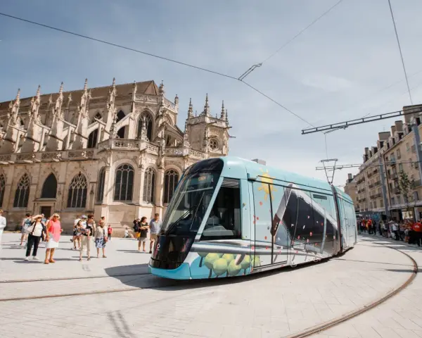 Un tram **Keolis Vélizy** décoré circule devant une cathédrale gothique. Des passants attendent sur le quai.