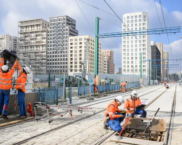 Des ouvriers travaillent sur de nouvelles infrastructures de tramway, avec des immeubles modernes en arrière-plan.