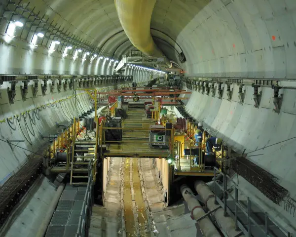 Intérieur d'un tunnel duplex en construction, avec des machines, des ouvriers et des tuyaux.
