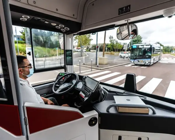 Vue de l'intérieur d'un bus RATP, le conducteur porte un masque. Un autre bus approche au loin.