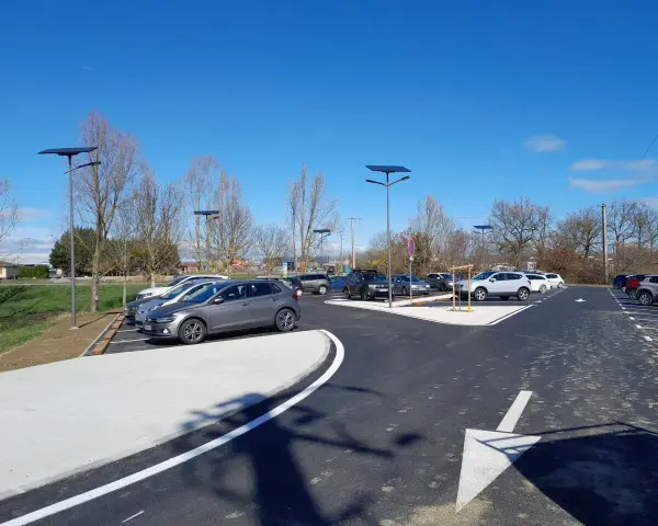 Stationnement de voitures dans une aire covoiturage Toulouse, éclairée par des lampadaires solaires sous un ciel bleu.