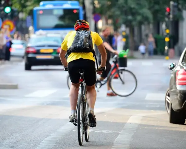 Un cycliste en tenue jaune et casque rouge profite de faire du vélo en ville, traversant une rue animée avec des voitures et un bus.