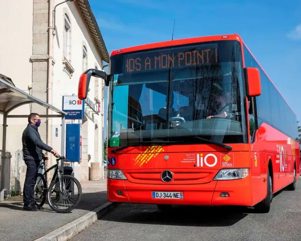 Un homme attend un bus LIO rouge à un arrêt, prêt à monter avec son vélo. Ce bus dessert les lignes comme Graulhet Gaillac.