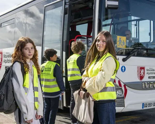 Trois jeunes, portant des gilets de sécurité fluo, attendent devant un bus scolaire de la Région Nouvelle-Aquitaine. La région vous transporte vers de nouvelles aventures.