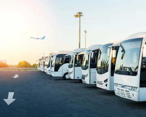 Une flotte de bus blancs alignés, prêts à transporter des passagers. L'avion au loin suggère la capacité d'un bus à relier les gens à leurs destinations.