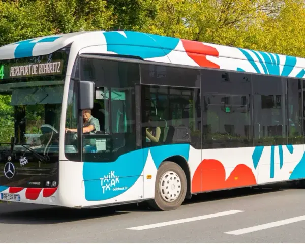 Bus txiktxak Bayonne, ligne 4, direction Aéroport de Biarritz, avec un motif coloré bleu et rouge sur fond blanc.