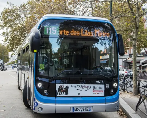 Bus Bolloré 115, direction Porte des Lilas Métro, stationné dans une rue bordée d'arbres et de commerces.