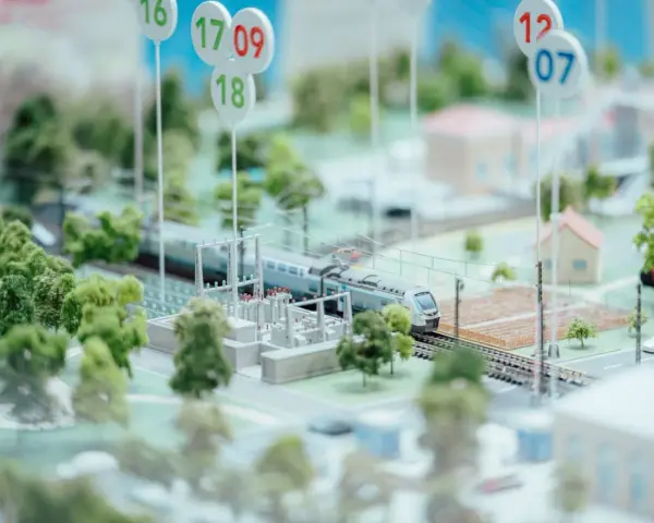 Maquette ferroviaire avec un train, des arbres et des maisons. Des panneaux indiquent des dates, peut-être pour un projet mobco 2026.