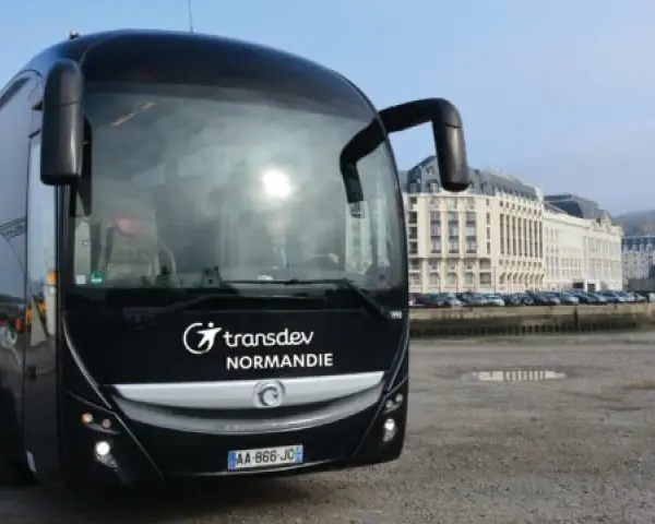 Autocar noir Transdev Normandie garé sur un quai, avec des bâtiments en arrière-plan.