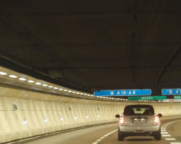 Voiture dans un tunnel éclairé, direction A10-A6 et A13. Un panneau indique Créteil et Versailles. Passage d'un duplex péage.