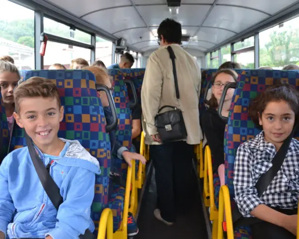 Des enfants souriants et une adulte voyagent dans un autobus scolaire aux sièges colorés.