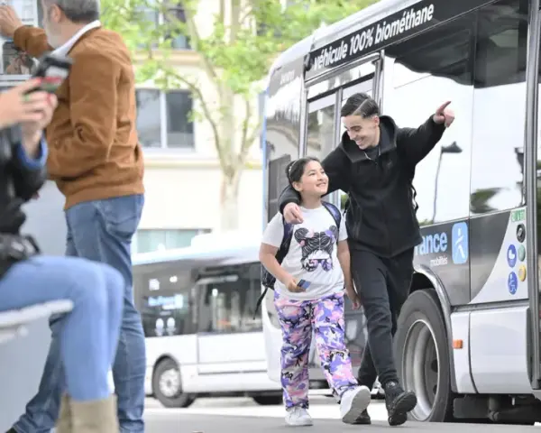 Un jeune homme et une fillette souriants marchent près d'un bus Transdev à Blois.