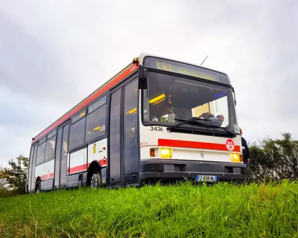 Un bus Renault R312 blanc et rouge, immatriculé FZ-609-NL, roule sur une colline herbeuse sous un ciel couvert.