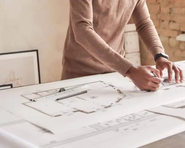 Un architecte dessine des plans détaillés, traçant des lignes précises pour un projet. Il y a plu trappes sur la table.