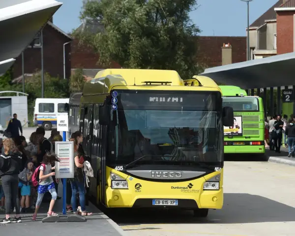 Des bus jaunes et verts attendent des passagers. Une affiche sur le bus vert mentionne "100% GRATUIT", illustrant la gratuité des transports en commun.