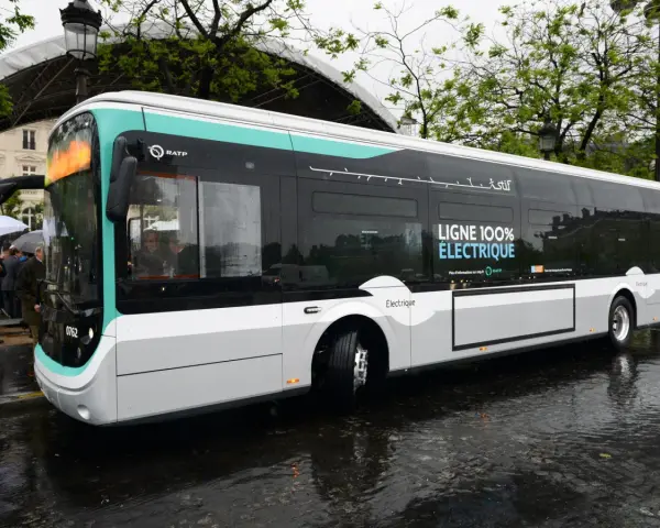 Un bus RATP bleu et blanc, "LIGNE 100% ÉLECTRIQUE", roule sur une chaussée mouillée.