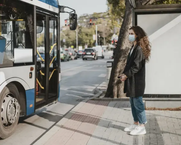 Une jeune femme avec un masque attend le bus, un moyen de déplacement pratique en ville.