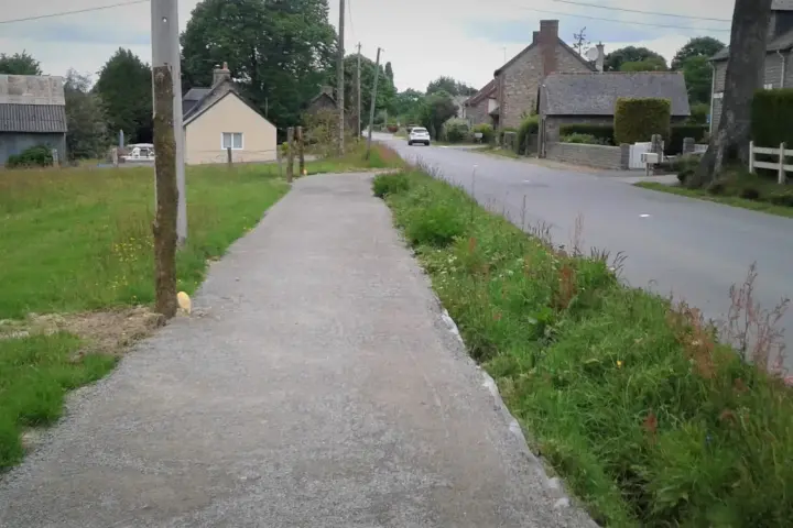 Un chemin de gravier longe une route de campagne bordée d'herbes folles. C'est un exemple de cheminement doux, invitant à la promenade paisible.